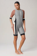 Woman wearing a colorblock rashguard bodysuit with front zipper and half sleeves, standing barefoot