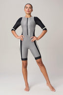 Woman in a gray and black athletic rash guard bodysuit with front zipper, standing barefoot.