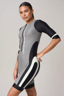 Woman wearing a grey and black short-sleeve athletic one-piece with front zipper detail.