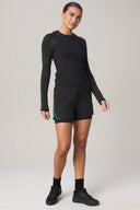 Woman in black long sleeve athletic top and charcoal workout shorts with side green detail
