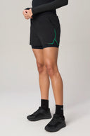 Charcoal athletic shorts with inner lining, green accent, worn by person standing indoors.