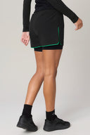Rear view of woman wearing charcoal athletic shorts with green trim and black sneakers