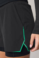 Close-up of charcoal athletic shorts with green trim and subtle logo, worn by a person