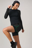 Woman in black athletic shorts with green trim, long sleeve top, and headphones posing actively