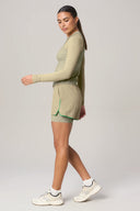 Woman in pale olive athletic shorts with green trim and long-sleeve top, side view