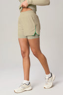 Woman wearing pale olive high-waisted athletic shorts with green trim and white sneakers