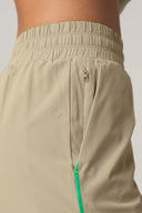 Close-up of pale olive athletic shorts with elastic waistband, zip pocket, and green trim detail