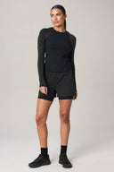 Woman wearing a charcoal long-sleeve active tee and black athletic shorts, studio background