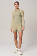 Woman wearing pale olive long sleeve active tee and shorts set, standing in studio