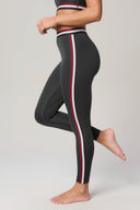 Side view of woman wearing charcoal leggings with red and white side stripes, barefoot