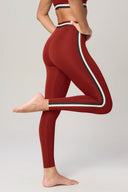 Woman wearing merlot red high-waisted leggings with side stripes, in yoga pose on grey background